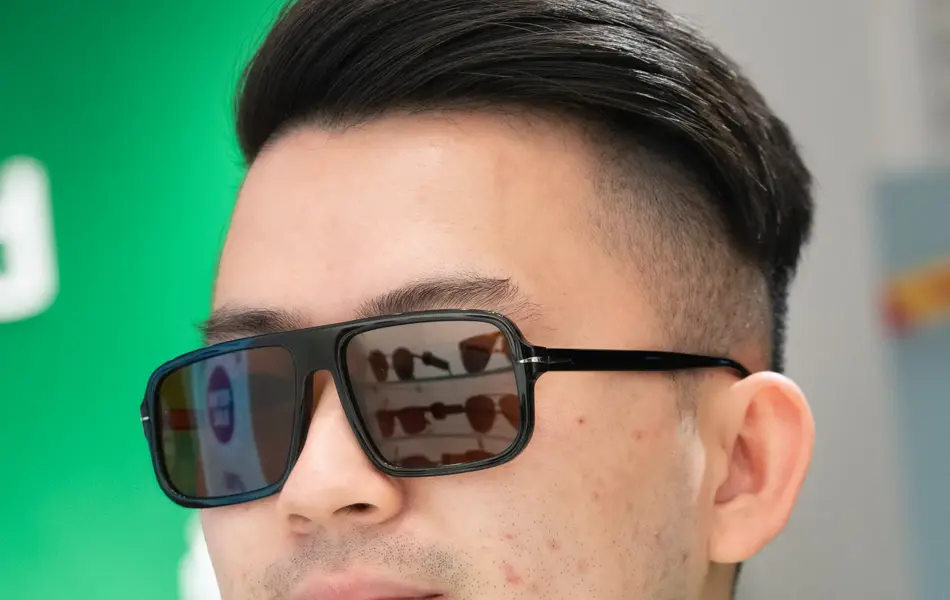 En gutt med mørkt kort hår som har på seg en grønn genser og sorte litt firkantede solbriller fra David Beckham