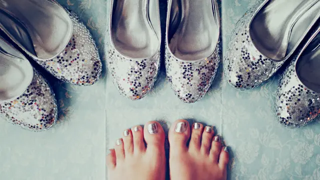 Nærbilde av føtter med metallisk neglelakk og tre par sølv ballerinasko med glitter