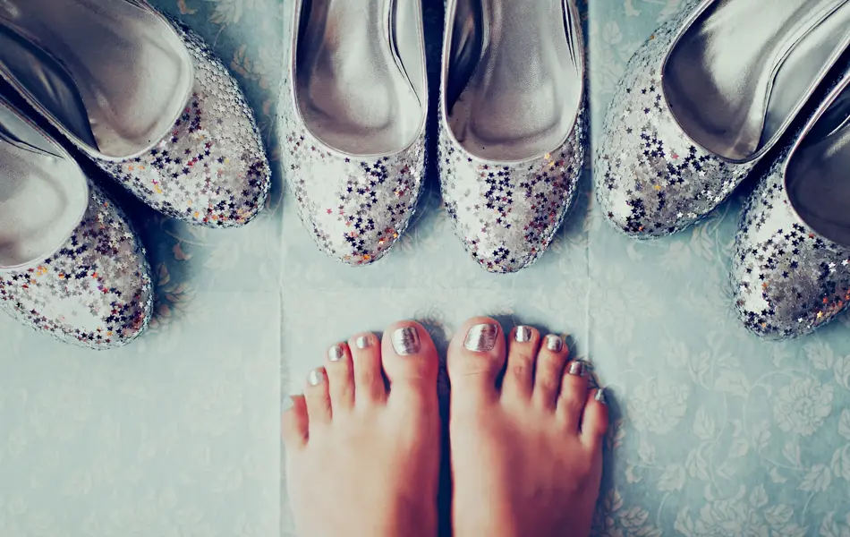 Nærbilde av føtter med metallisk neglelakk og tre par sølv ballerinasko med glitter