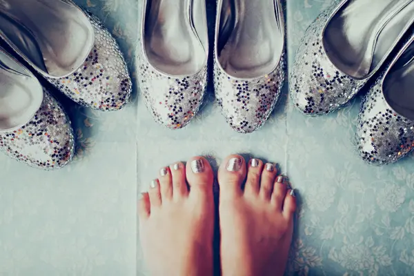 Nærbilde av føtter med metallisk neglelakk og tre par sølv ballerinasko med glitter