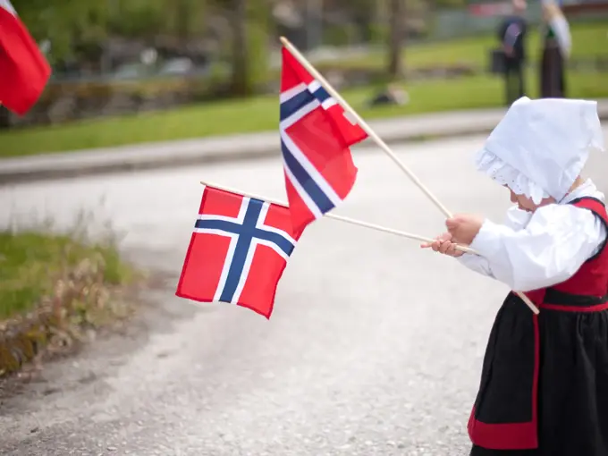 Jente i drakt feirer med to norgesflagg på 17. mai