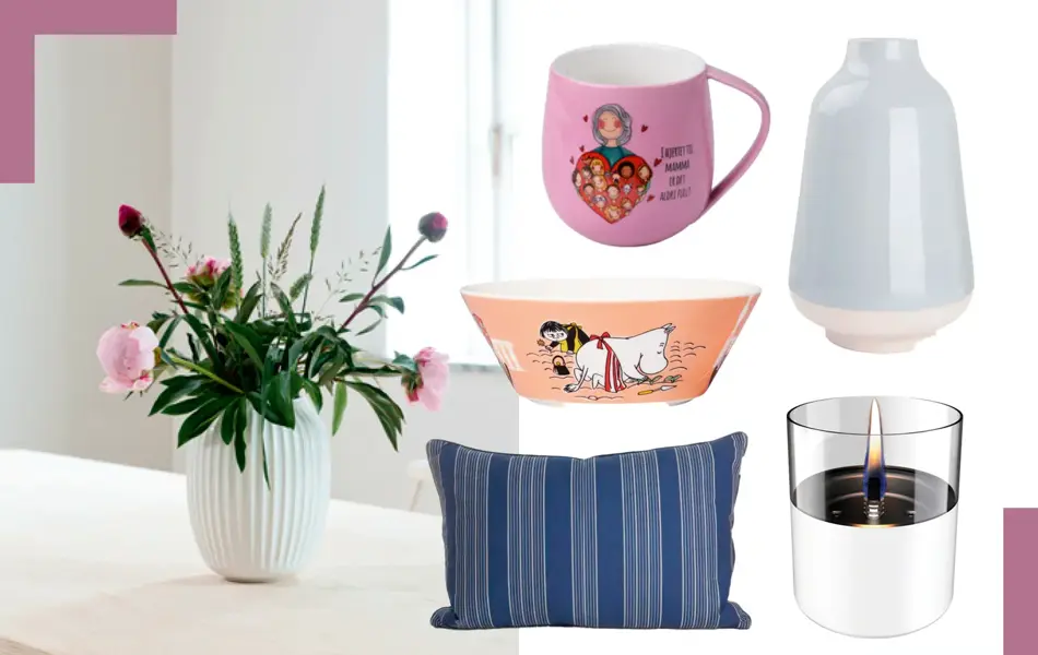 Kähler vase med blomster på et bord, rosa krus, lyseblå vase, Mummie-bolle, blåstripete pute og bordlykt.