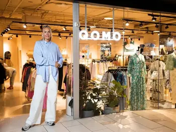 Dame i hvit bukse og blå skjorte står utenfor inngangen til butikk på kjøpesenter.