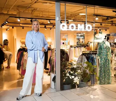 Dame i hvit bukse og blå skjorte står utenfor inngangen til butikk på kjøpesenter.