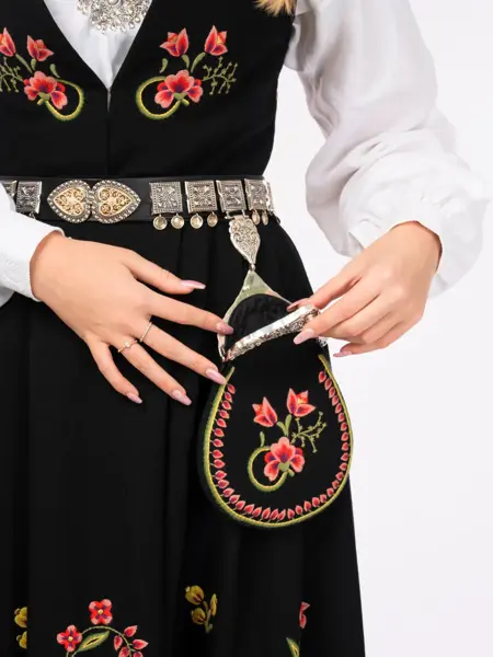 Jente med svart bunad viser frem bunadsvesken