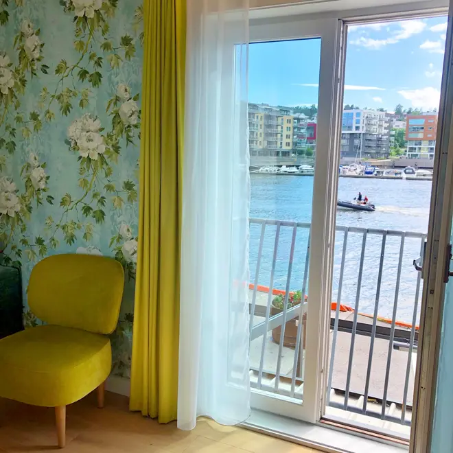 Rom hos Thon Hotel Tønsberg Brygge med gulv til tak-vindu, mønstrete tapet, gul stol og parkettgulv.