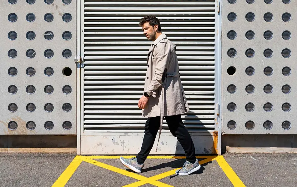 Mann i lys trenchcoat går inntil vegg med mønster 