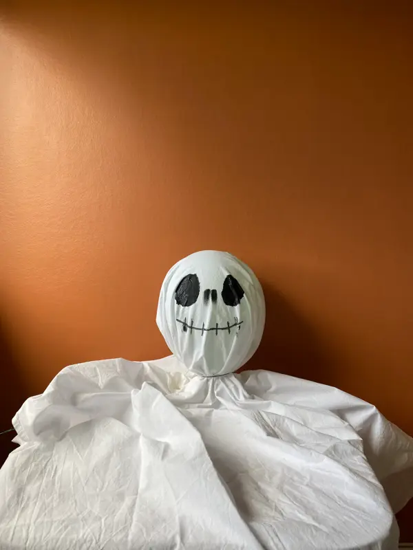 Oppblåst ballong inni et laken med tegnet ansikt som ligger på et bord med oransje bakgrunn