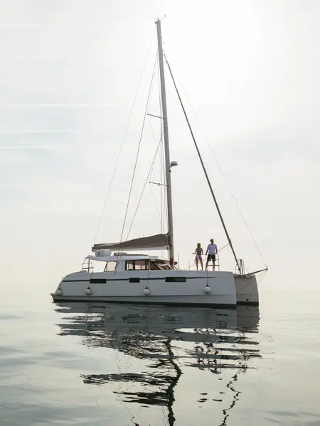 Hvit seilbåt på stille vann med disig himmel