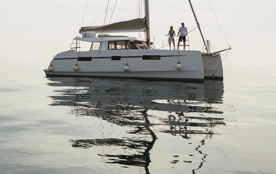Hvit seilbåt på stille vann med disig himmel