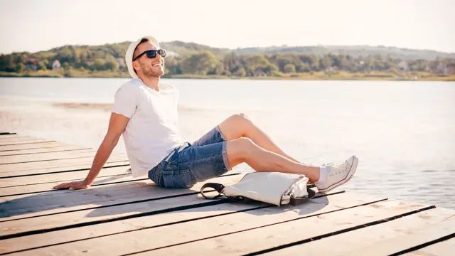 Young man sitting at the pier and enjoys in nature and sun.
