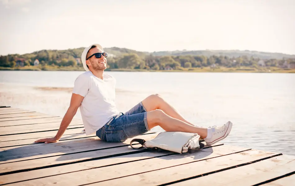 Young man sitting at the pier and enjoys in nature and sun.