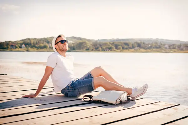 Young man sitting at the pier and enjoys in nature and sun.