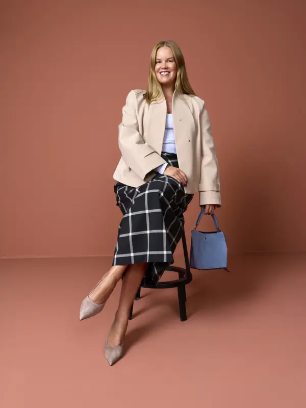 Elen med beige dressjake, rutet skjørt, pumps og blå veske.