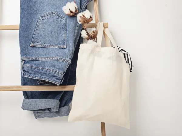 Jeans henger på en stige sammen med et handlenett med bombullsblomst i.