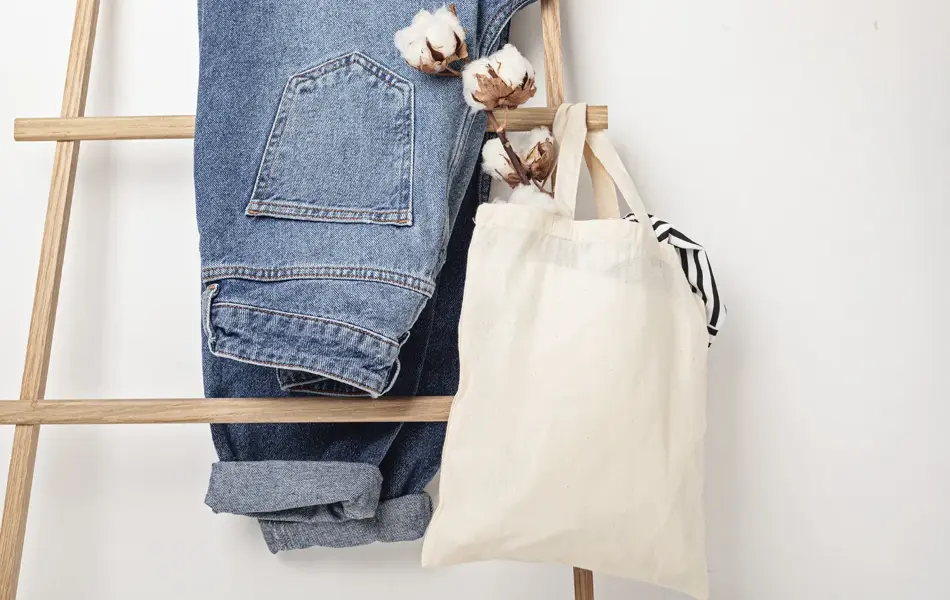 Jeans henger på en stige sammen med et handlenett med bombullsblomst i.