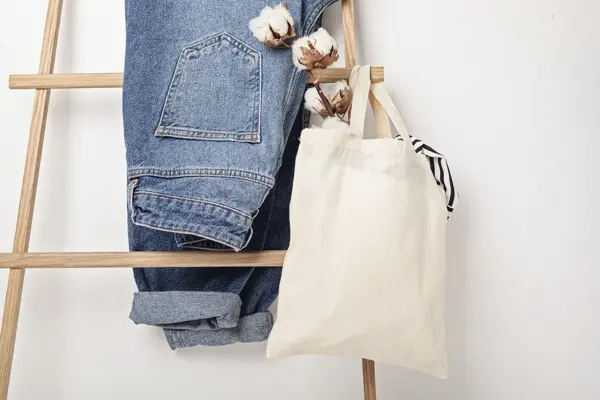 Jeans henger på en stige sammen med et handlenett med bombullsblomst i.