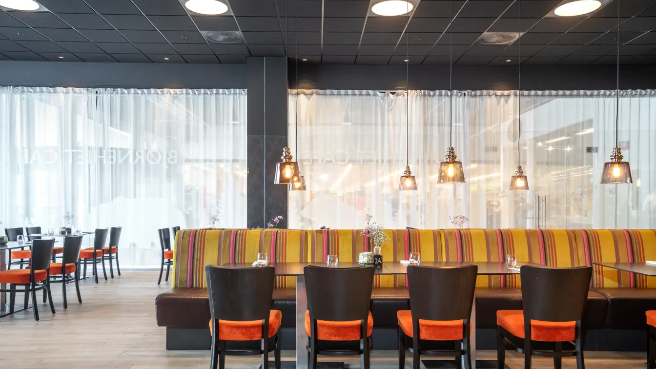 Parkettgulv, vindu, spisesofa, oransje stoler, svarte bord, svarte vegger.