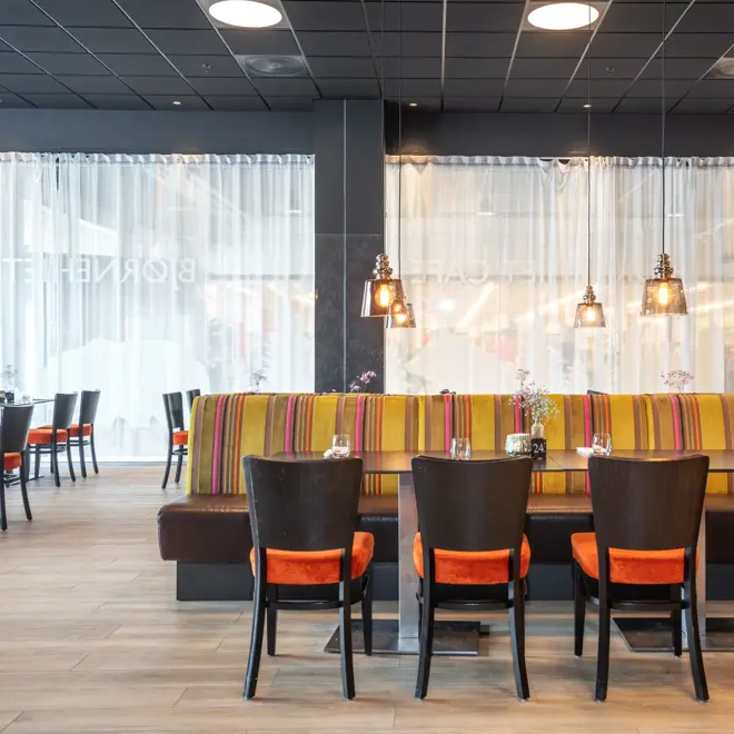 Parkettgulv, vindu, spisesofa, oransje stoler, svarte bord, svarte vegger.