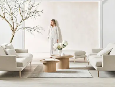 dame som poserer mot veggen i en lys stue med tre, sofa, bord, puff og lampe