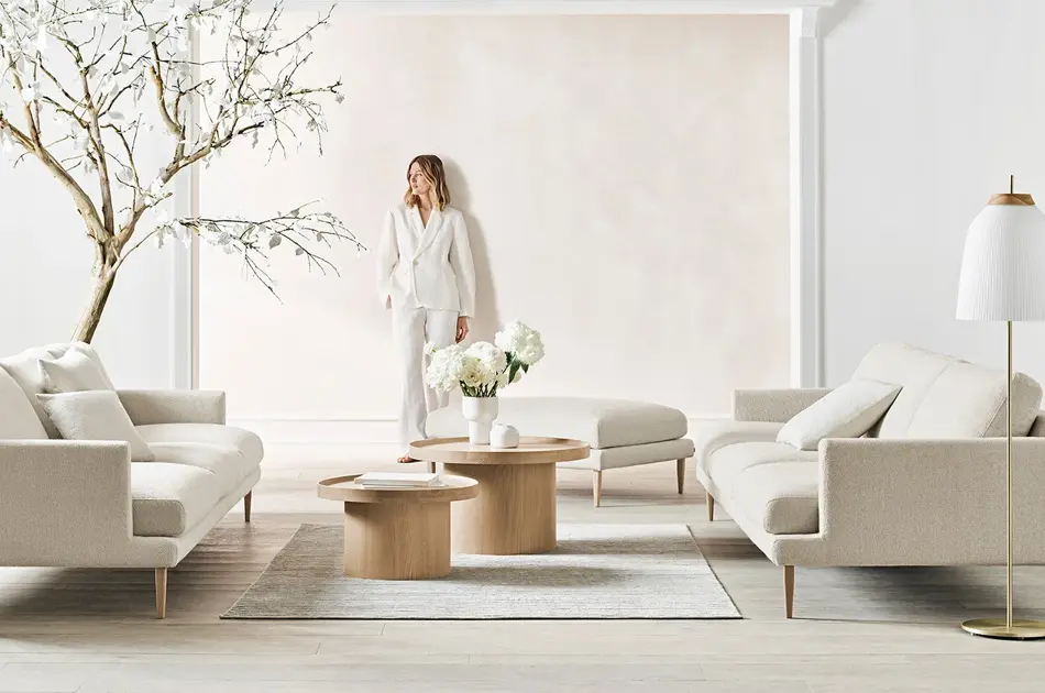 dame som poserer mot veggen i en lys stue med tre, sofa, bord, puff og lampe