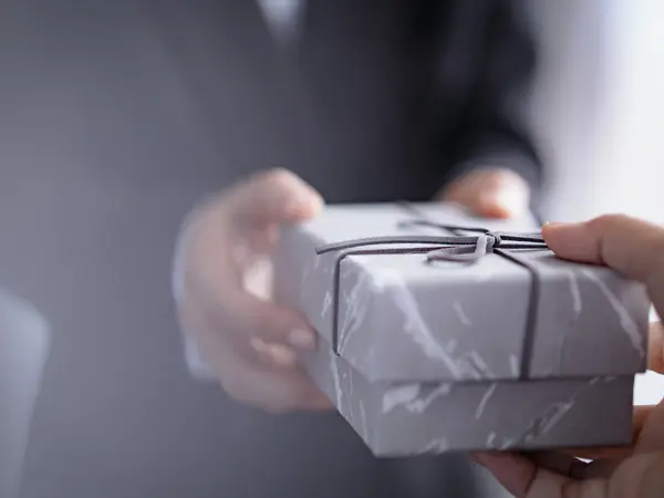 Person i dress tar imot pakke, fokus på hender, uskarp bakgrunn. Foto til artikkel om ting å huske på når du skal arrangere konfirmasjon,
