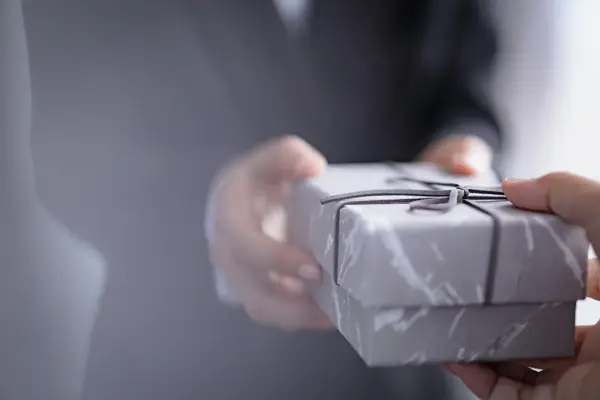 Person i dress tar imot pakke, fokus på hender, uskarp bakgrunn. Foto til artikkel om ting å huske på når du skal arrangere konfirmasjon,