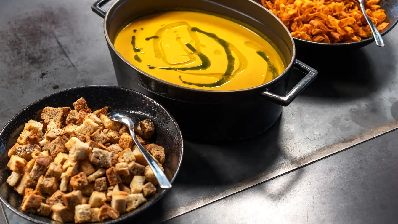 Kveldsmat på buffet. Kjele med gul suppe og to boller med suppetilbehør på hver side.