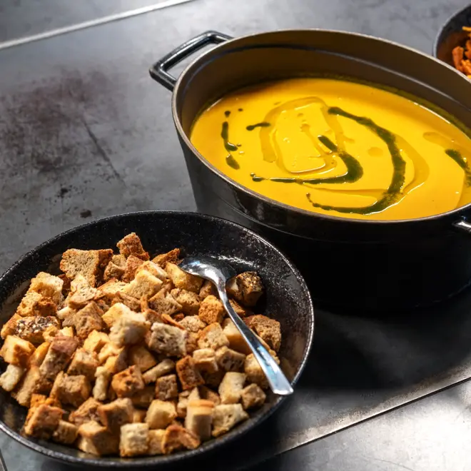 Kveldsmat på buffet. Kjele med gul suppe og to boller med suppetilbehør på hver side.