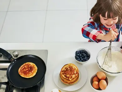 Gutt rører i pannekakerøre på kjøkken ved stekepanne, egg og blåbær