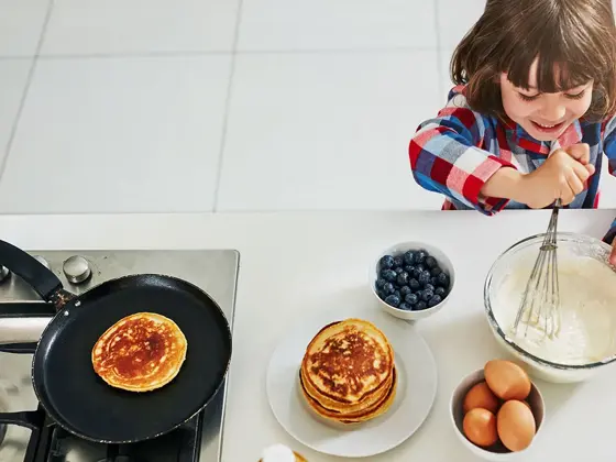 Gutt rører i pannekakerøre på kjøkken ved stekepanne, egg og blåbær