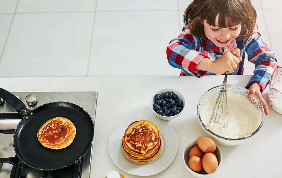 Gutt rører i pannekakerøre på kjøkken ved stekepanne, egg og blåbær