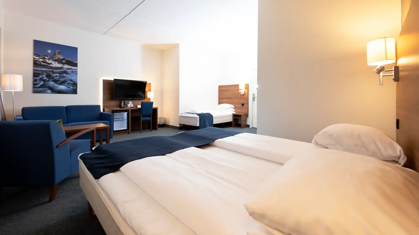 En dobbeltseng, en enkeltseng, sofagruppe og TV i familierom