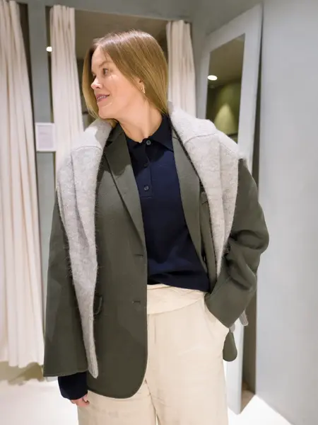 Damemed hvit bukse, blå skjorte, grønn dressjakke og strikkegenser over skuldre