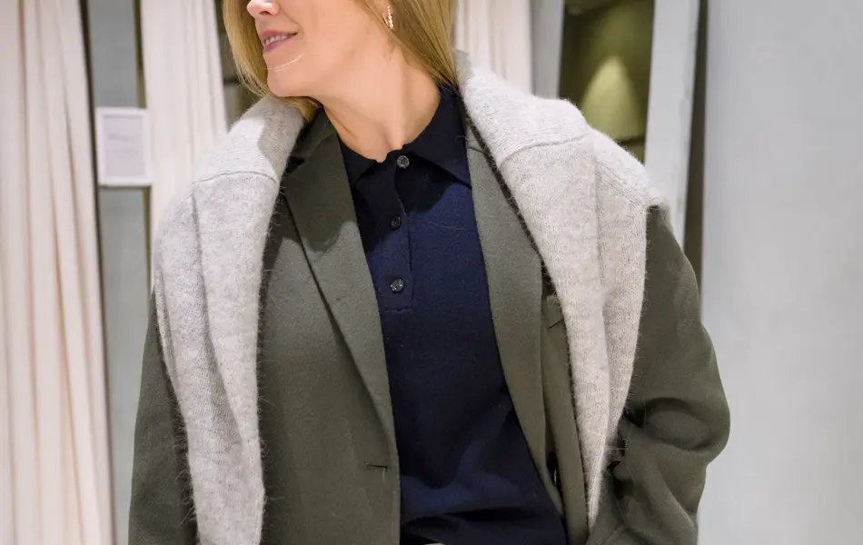 Damemed hvit bukse, blå skjorte, grønn dressjakke og strikkegenser over skuldre