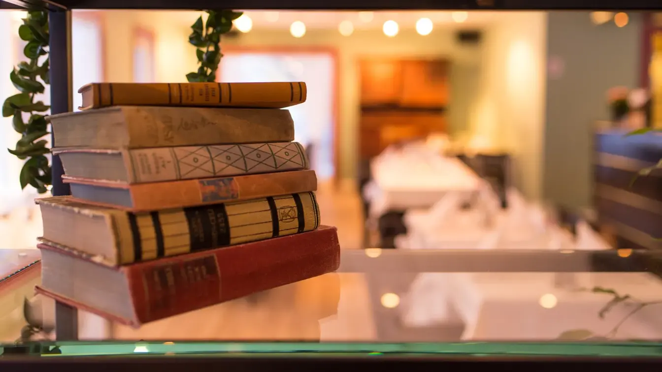 Lykt med lys og bokhylle med plante og bøker med restaurant Jegerstugu Cafe & Bar i bakgrunnen på Thon Hotel Hallingdal