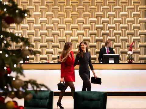 To smilende gjester i penklær går gjennom lobby foran resepsjonsdisk.