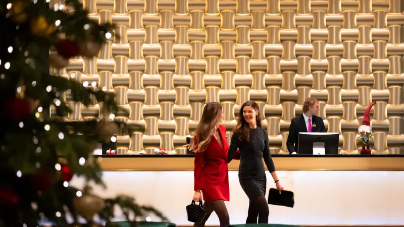 To smilende gjester i penklær går gjennom lobby foran resepsjonsdisk.