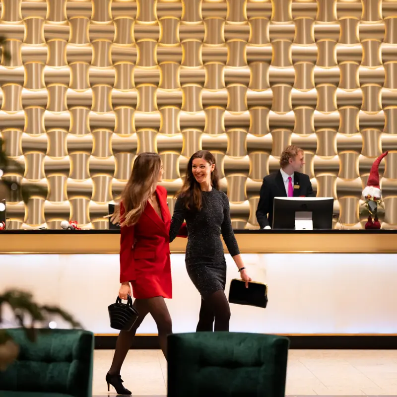 To smilende gjester i penklær går gjennom lobby foran resepsjonsdisk.