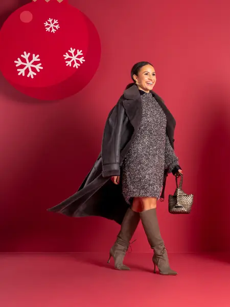 Mona Berntsen i skimrende grå kjole, støvletter, veske og sort kåpe.