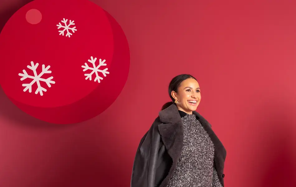 Mona Berntsen i skimrende grå kjole, støvletter, veske og sort kåpe.