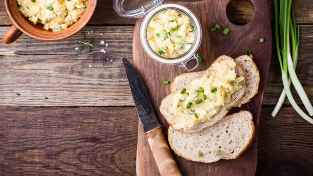 Egg paste sandwich with spring green onion for healthy and delicious brunch on rustic wooden cutting board viewed from above