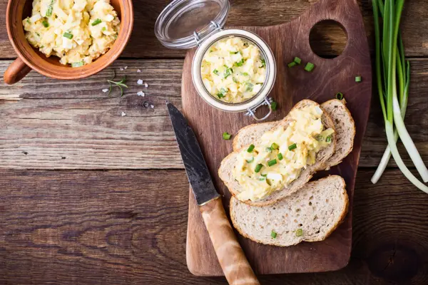 Egg paste sandwich with spring green onion for healthy and delicious brunch on rustic wooden cutting board viewed from above