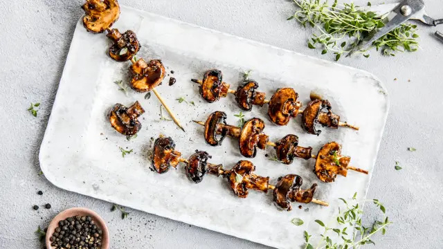 Grillspyd med grillet sopp på hvitt fat med urter rundt