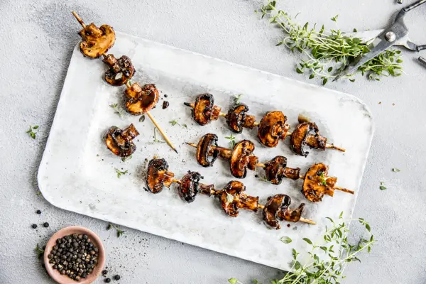 Grillspyd med grillet sopp på hvitt fat med urter rundt