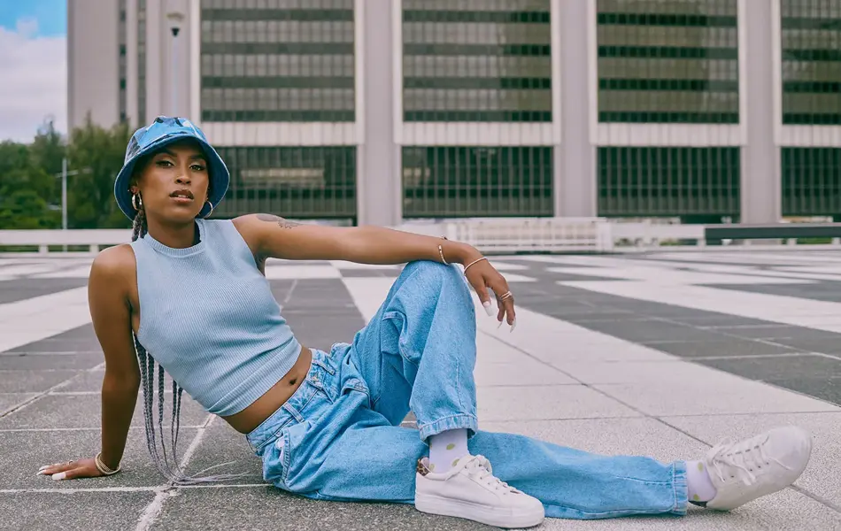 Kvinne med jeans og bøttehatt poserer på bakken utendørs