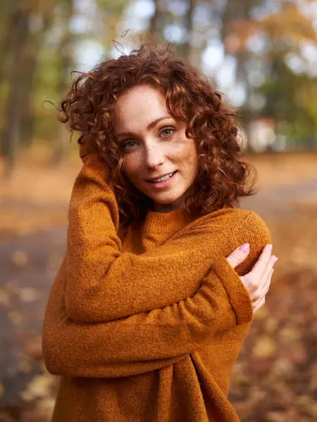 En dame med brun strikkegenser står i en park