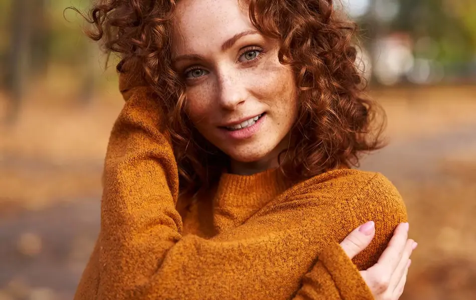 En dame med brun strikkegenser står i en park