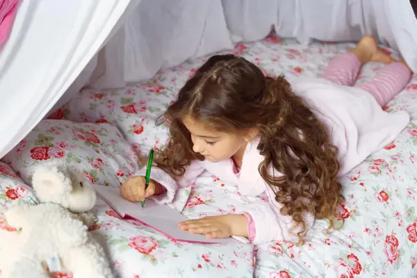 Jente som tegner ligger i seng med blomstrete sengetøy 