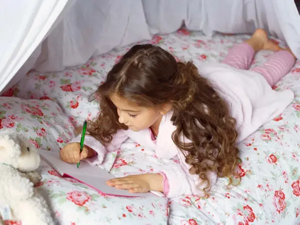 Jente som tegner ligger i seng med blomstrete sengetøy 